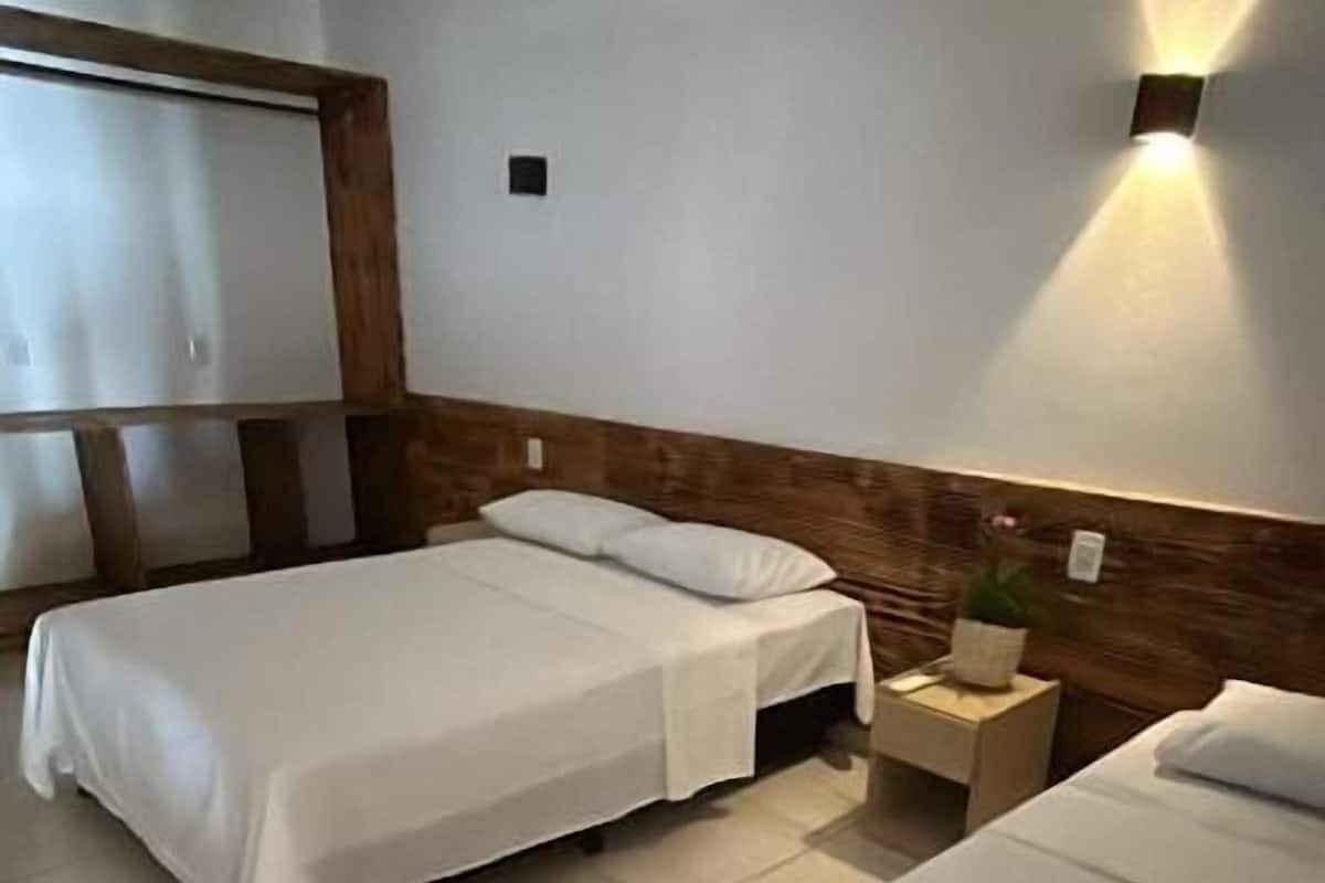 A hotel room with two beds, a wooden headboard, a nightstand with a lamp, and a small potted plant.