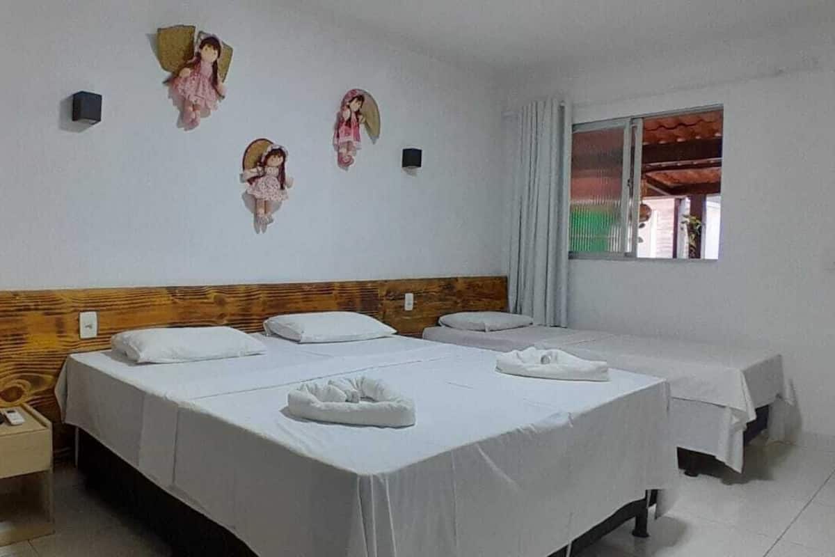 A hotel room with two beds, a wooden headboard, a small bedside table, and a window with curtains.