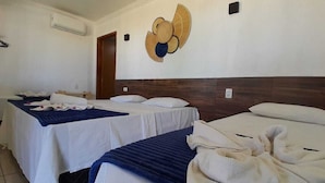 A hotel room with two beds, each with a blue bedspread and white linens. There is a wall-mounted fan and a decorative wall piece above the beds. - Pousada Villa Mar Porto (Ipojuca)