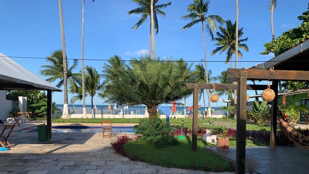 A patio area with a stone pathway, a wooden pergola, and a palm tree. - Pousada Villa Mar Porto (Ipojuca)