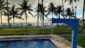 A swimming pool with a blue tile border, surrounded by a grassy area and palm trees. - Pousada Villa Mar Porto (Ipojuca)