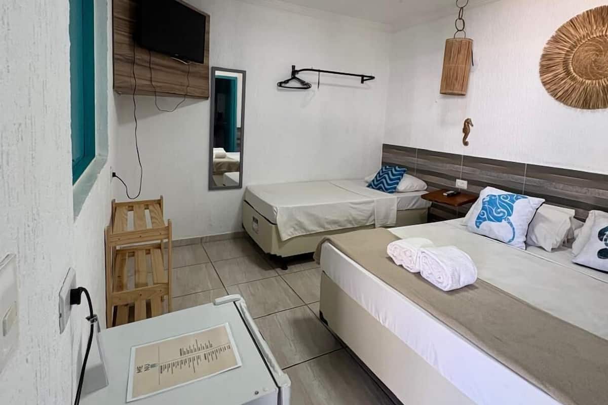 A hotel room with a bed, a desk, a mirror, a hanging light fixture, and a small window.
