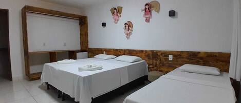 Habitación con tres camas, cada una con ropa blanca y almohadas. Figuras de ángeles decorativas fijadas en la pared.