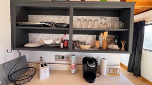 A kitchen with a black shelf holding kitchenware, a kettle, and a coffee maker. - Alarcon Ranch  (Weldon)