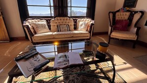 A room with a sofa, a chair, a glass coffee table, and a view of mountains through large windows. - Alarcon Ranch  (Weldon)