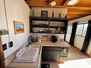 Une cuisine équipée d’un évier, d’une machine à café et d’une étagère contenant divers ustensiles de cuisine.