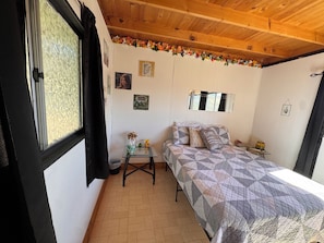 Une chambre à coucher avec un lit, une petite table, un miroir et une fenêtre avec des rideaux.