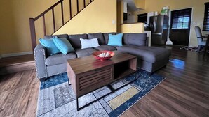 Ein Wohnzimmer mit Ecksofa, Couchtisch aus Holz und einer Treppe.