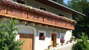 A two-story building with a wooden balcony adorned with flowers, a white facade, and a wooden door. - Apartment in Schwalbenhof Farm (Sankt Stefan im Rosental)