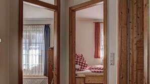 A hallway with wooden flooring leading to a bedroom with a bed and a window with curtains. - Apartment in Schwalbenhof Farm (Sankt Stefan im Rosental)