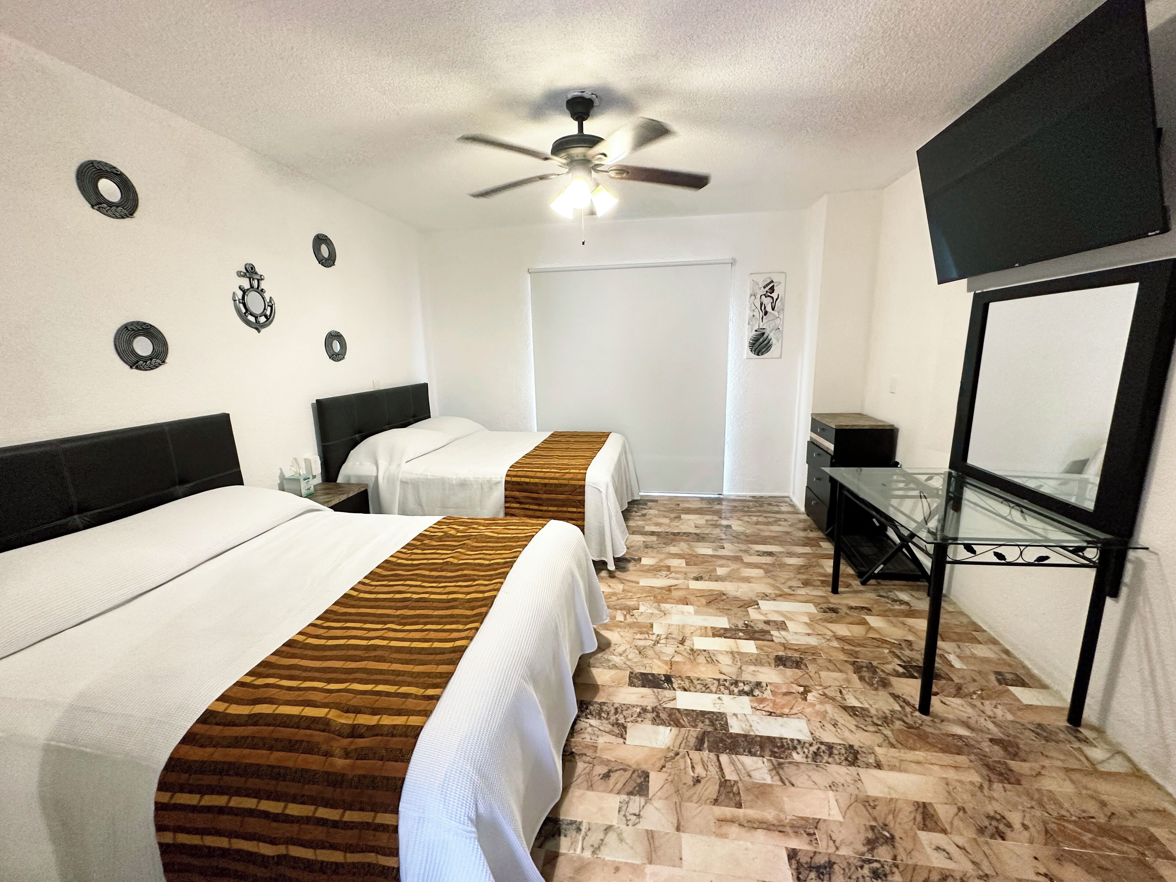 A hotel room with two beds, a ceiling fan, a TV, and a desk.