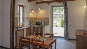 A kitchen with wooden beams, a dining table with chairs, a microwave, and a window with a view of the outside. - Apartment in Casola Near Torre di Casola (Casola in Lunigiana)