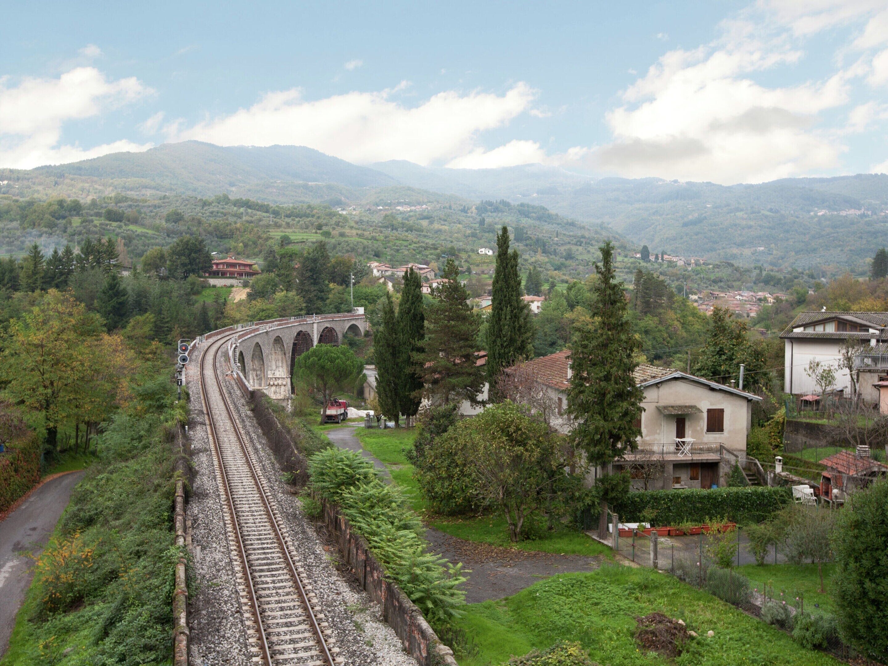 A railway track with a bridge, surrounded by greenery and houses.
