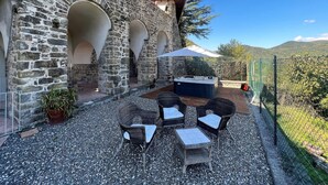 An outdoor patio with stone walls, a hot tub, wicker furniture, and a view of the hills. - Apartment in Casola Near Torre di Casola (Casola in Lunigiana)