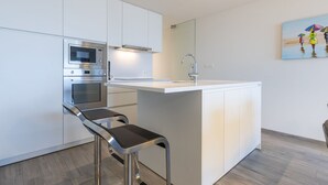 Een moderne keuken met witte kastjes, een inbouwoven, een magnetron, een roestvrijstalen barkruk en een schilderij aan de muur.