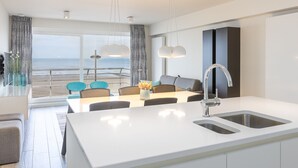Een moderne keuken met een groot eiland, een eetgedeelte met uitzicht op zee, en een balkon met een balustrade.