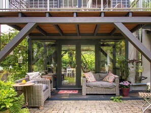 Un patio cubierto con muebles de mimbre, una puerta de cristal y vistas al exterior con vegetación.