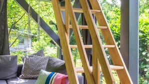Ein modernes Interieur mit einem grauen Sofa, bunten Kissen und einer Holzleiter.