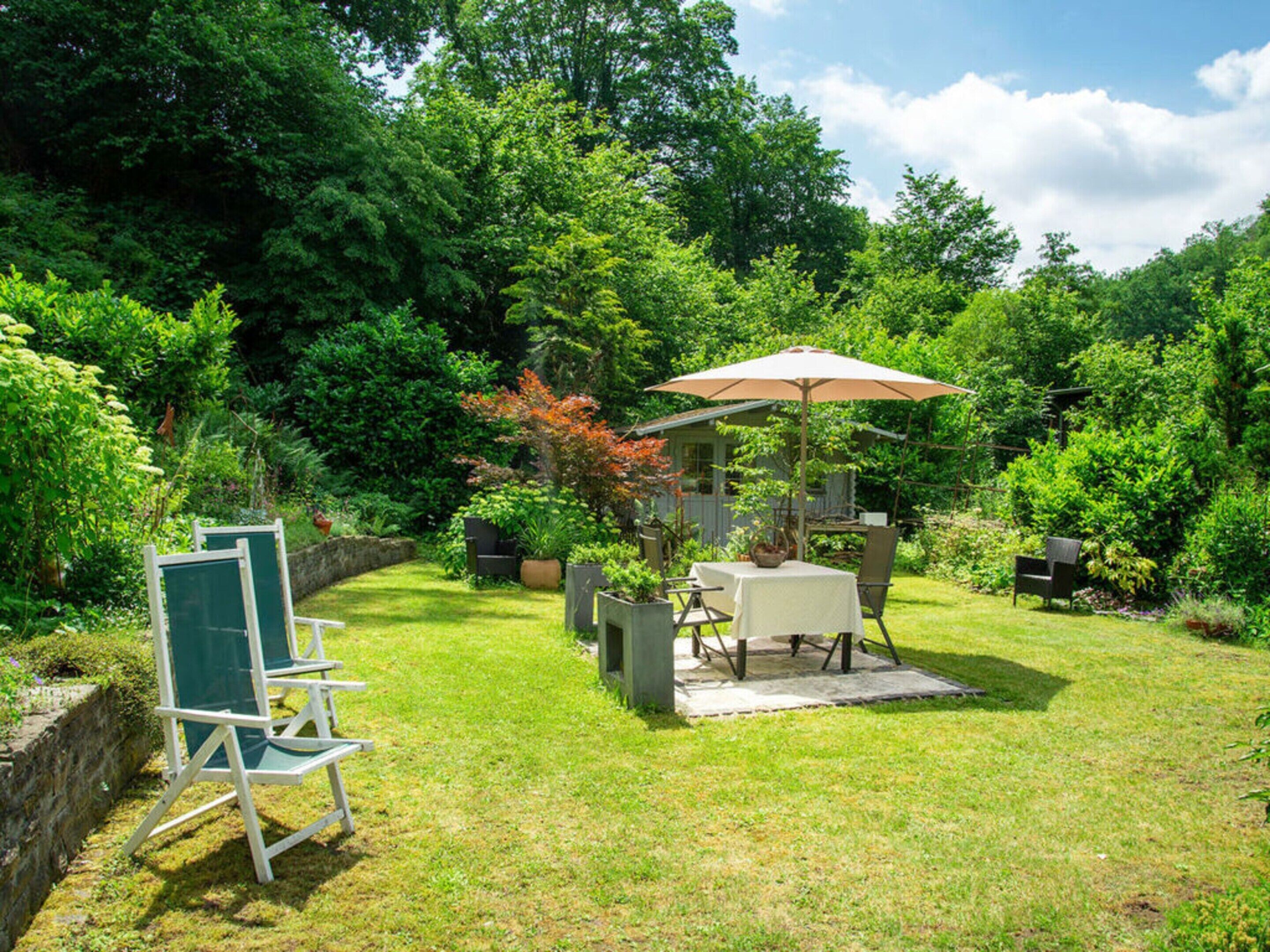 A patio area with a table and chairs, surrounded by lush greenery and trees.