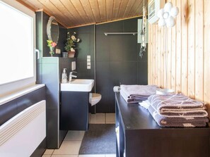 Un baño moderno con techo de madera, un lavabo negro, un inodoro y un perchero con toallas dobladas.