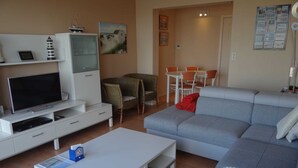 A modern living room with a grey sofa, white entertainment unit, and wicker chairs. - Apartment in Nieuwpoort With Views (Nieuwpoort)