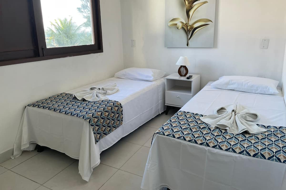 A hotel room with two single beds, a nightstand with a lamp, and a wall-mounted artwork.