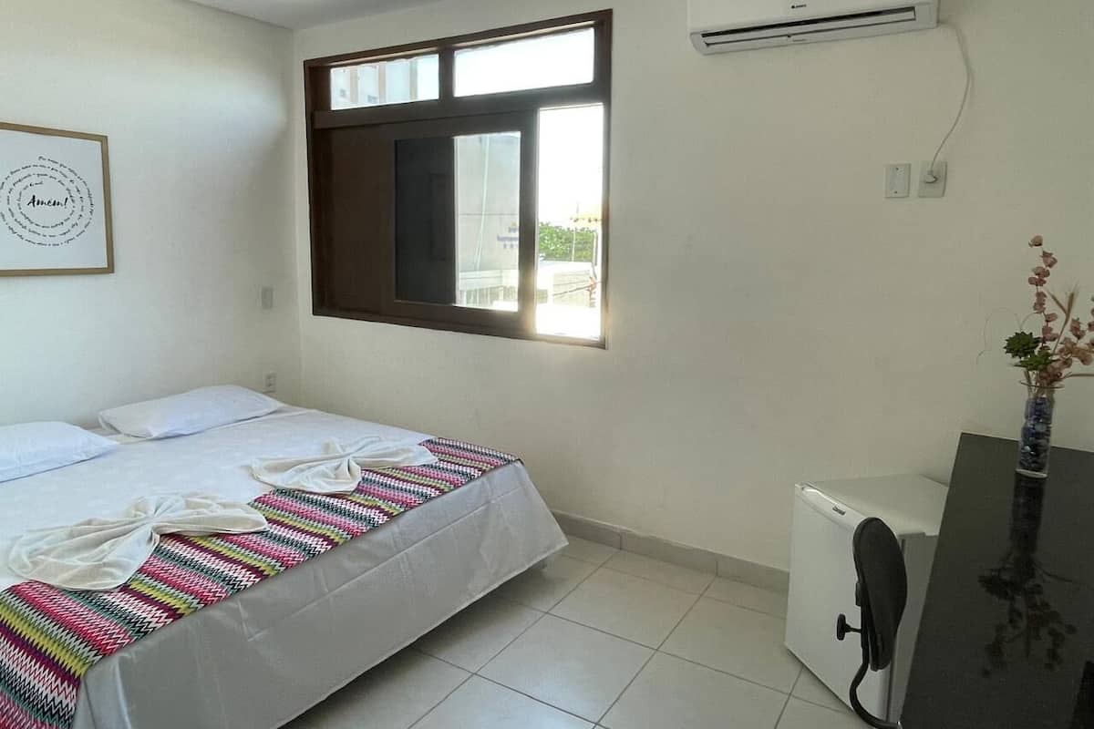 A hotel room with a bed, a desk, an air conditioner, and a window with a view.