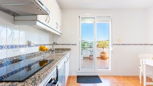 Une cuisine avec des meubles blancs, un plan de travail en granit et une vue sur un balcon agrémenté de plantes en pot.