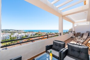 Een balkon met uitzicht op zee, ingericht met rieten stoelen en een tafel, en een fles wijn.