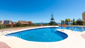 Une piscine au design incurvé, entourée d’une terrasse carrelée et d’une clôture.