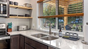 A kitchen with a double sink, stainless steel appliances, wooden shelves, and a window with blinds. - Base Camp | Lookout Lodge #2 (Big Prairie Township)
