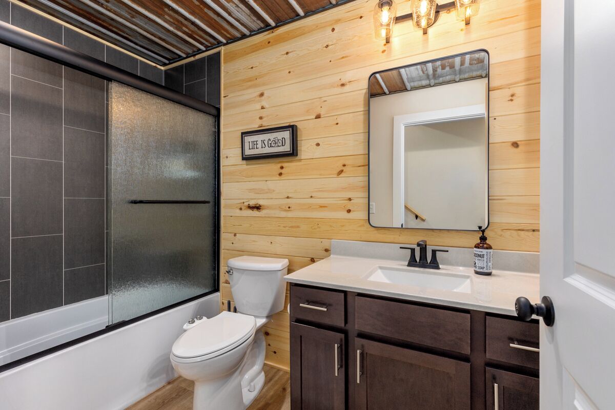 Un baño con pared de madera, inodoro blanco, lavamanos y espejo.