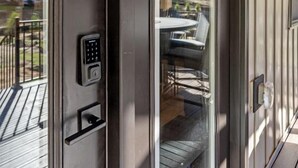 A modern exterior with a sliding glass door, a keypad lock, and a small outdoor seating area visible through the door. - Base Camp | Lookout Lodge #2 (Big Prairie Township)