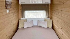 A narrow room with wooden walls, a bed with a textured mattress, a window with curtains, and a ceiling light fixture. - Ahoy Masal Modern Retreat (Lübeck)