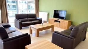 A modern living room with a sofa set, a coffee table, and a TV on a wooden cabinet. - Apartment in Nieuwpoort With Ocean Views (Nieuwpoort)