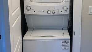 A compact washer and dryer unit in a small laundry room with a white door and wooden floor.