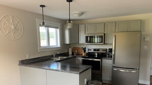A modern kitchen with a central island, stainless steel appliances, and light grey cabinetry.