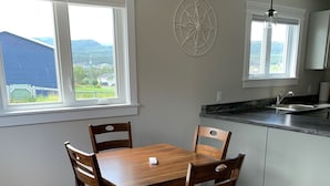 A dining area with a wooden table and chairs, a kitchen with a sink and countertop, and a compass wall decoration.