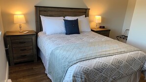 A neatly made bed with a patterned bedspread, two bedside lamps, a wooden nightstand with drawers, and a digital clock.