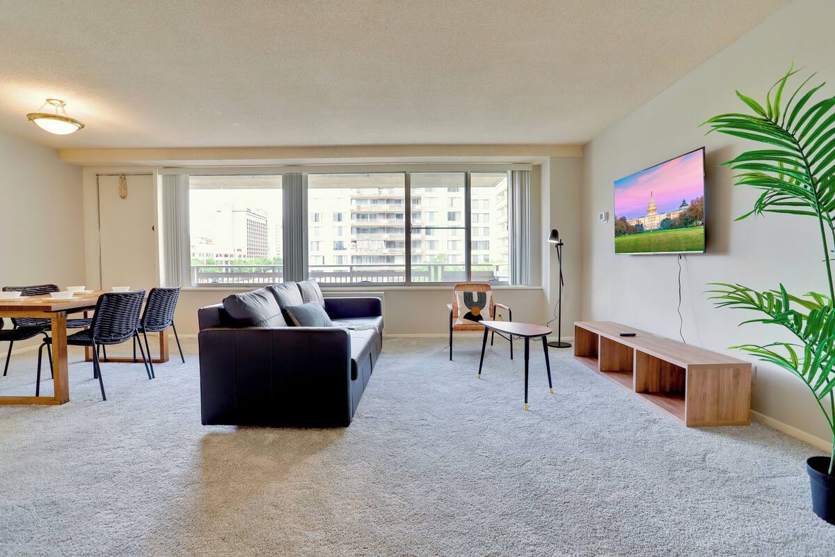Un salon moderne comprenant un canapé, des fauteuils, une table à manger et une grande fenêtre donnant sur la ville.
