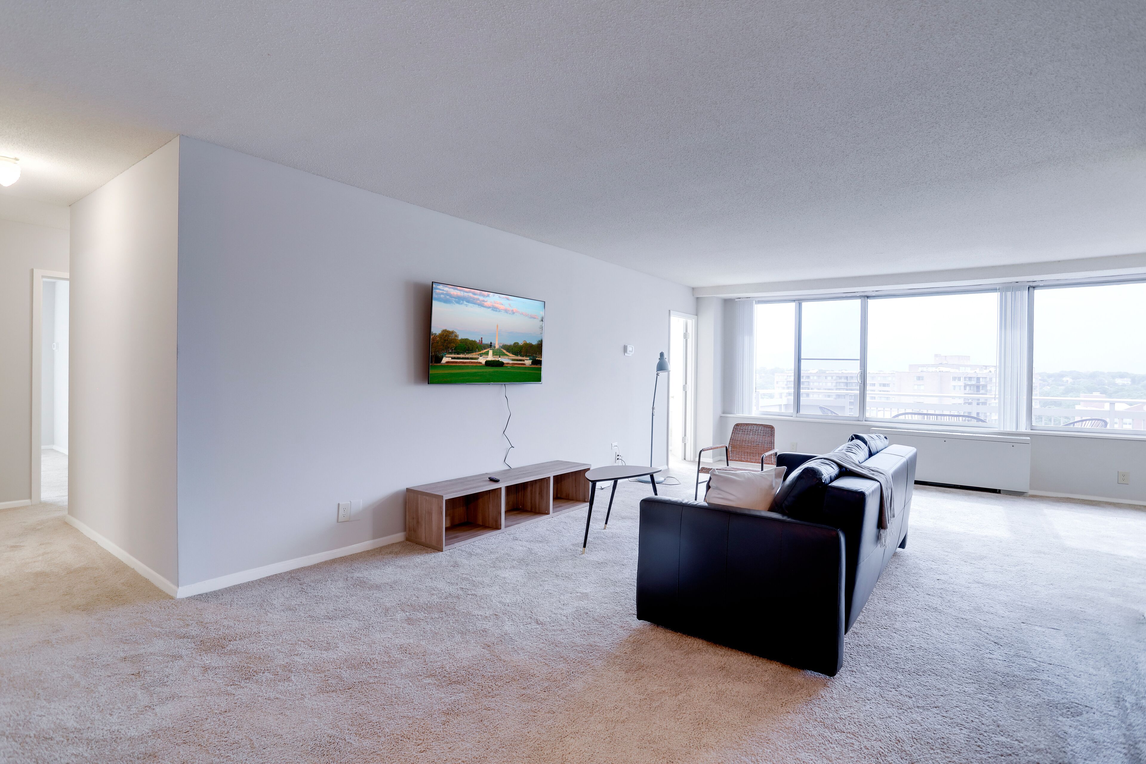 A modern living room with a flat-screen TV mounted on the wall, a black sofa, a coffee table, and a bench.