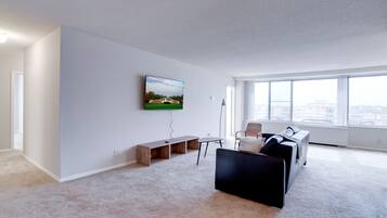 A modern living room with a flat-screen TV mounted on the wall, a black sofa, a coffee table, and a bench.