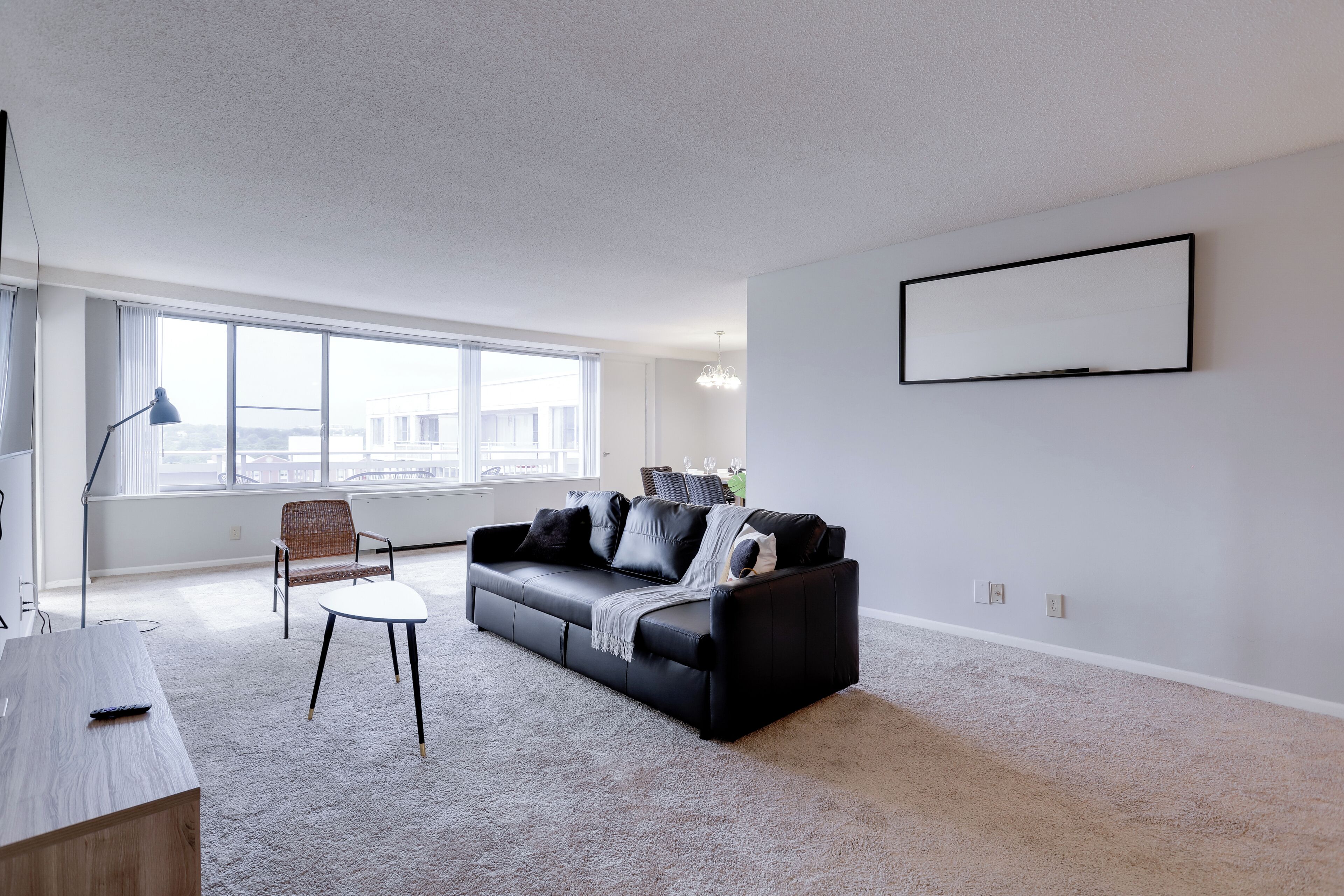 Una sala de estar moderna con un sofá de cuero negro, una mesa de centro blanca y un sillón gris. Hay un ventanal que proporciona luz natural y vistas a la ciudad.