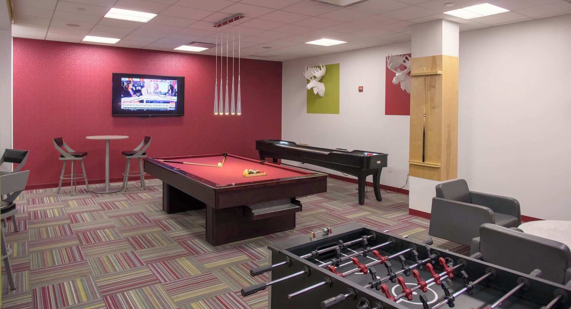 Une pièce équipée d’une table de billard, d’un baby-foot et d’un téléviseur diffusant un programme d’information.