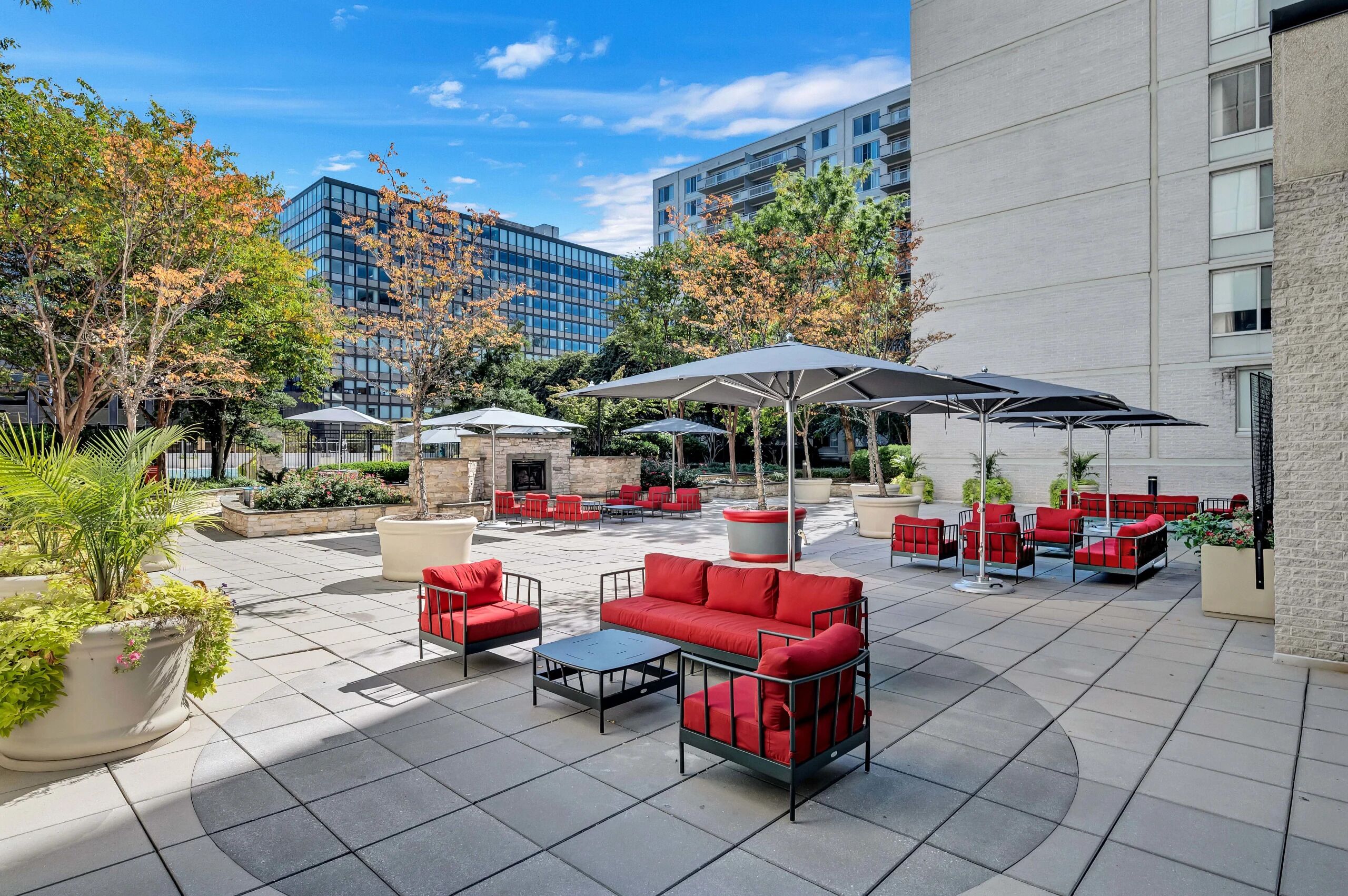An outdoor patio area with red and black outdoor furniture, umbrellas, and potted plants.
