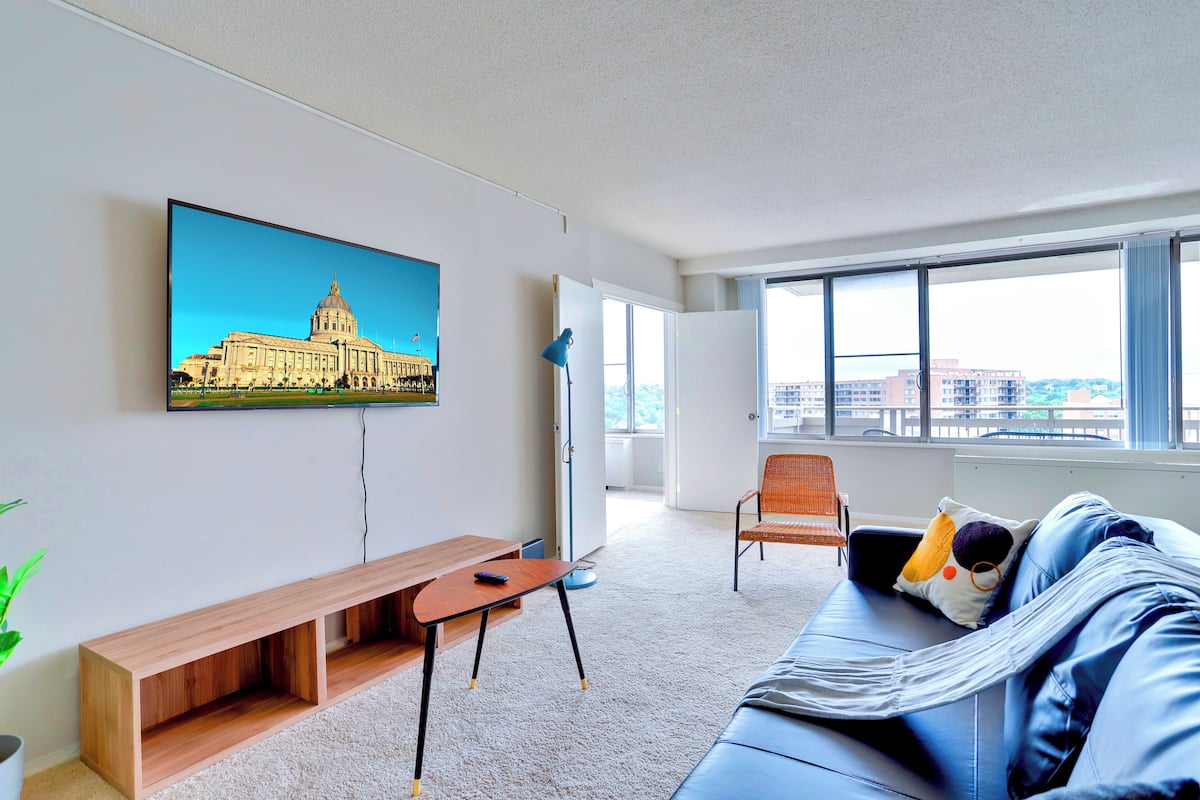 Un salon moderne avec un grand téléviseur fixé au mur, un canapé, un fauteuil et une petite table.