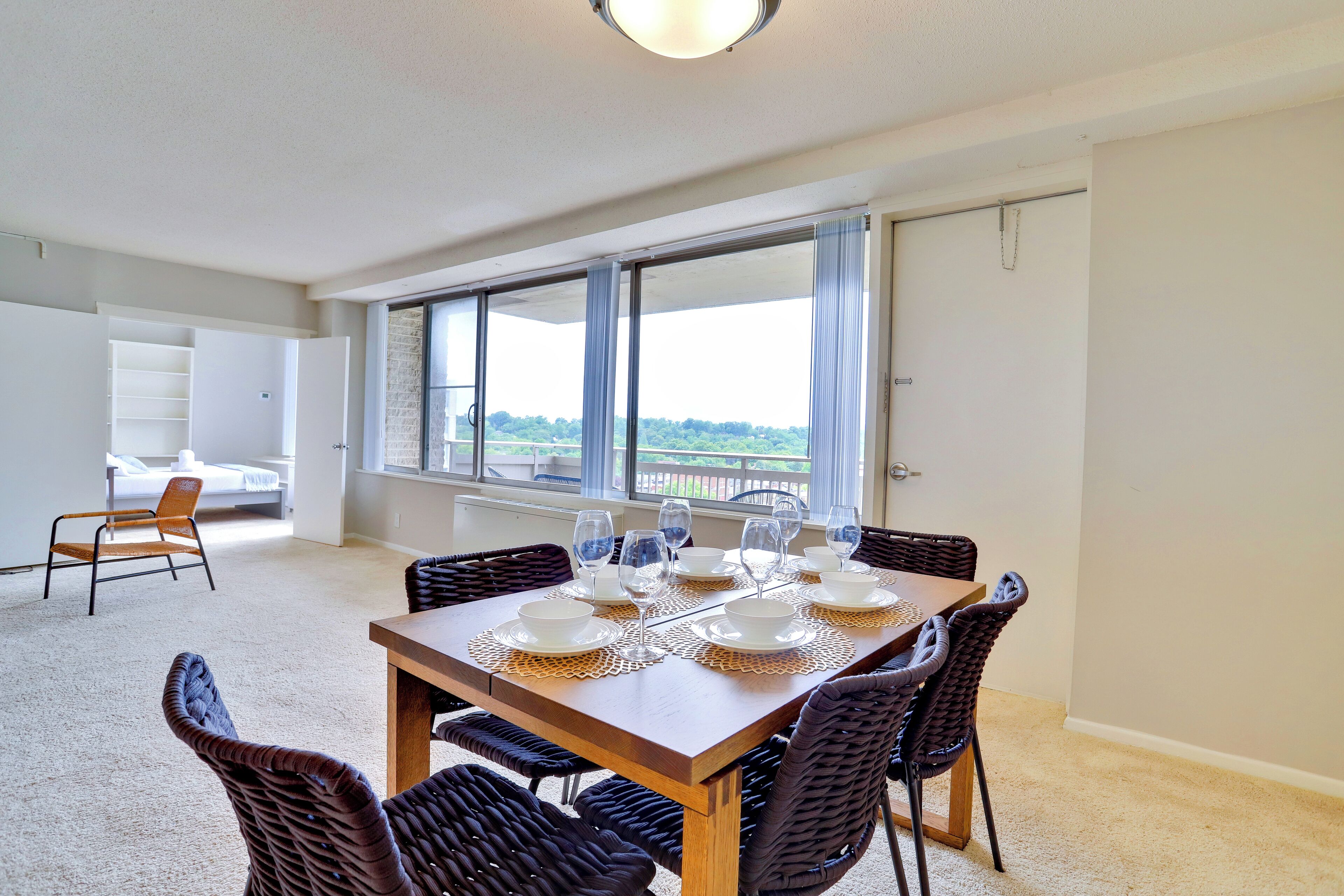A dining area with a wooden table set for six, surrounded by wicker chairs.