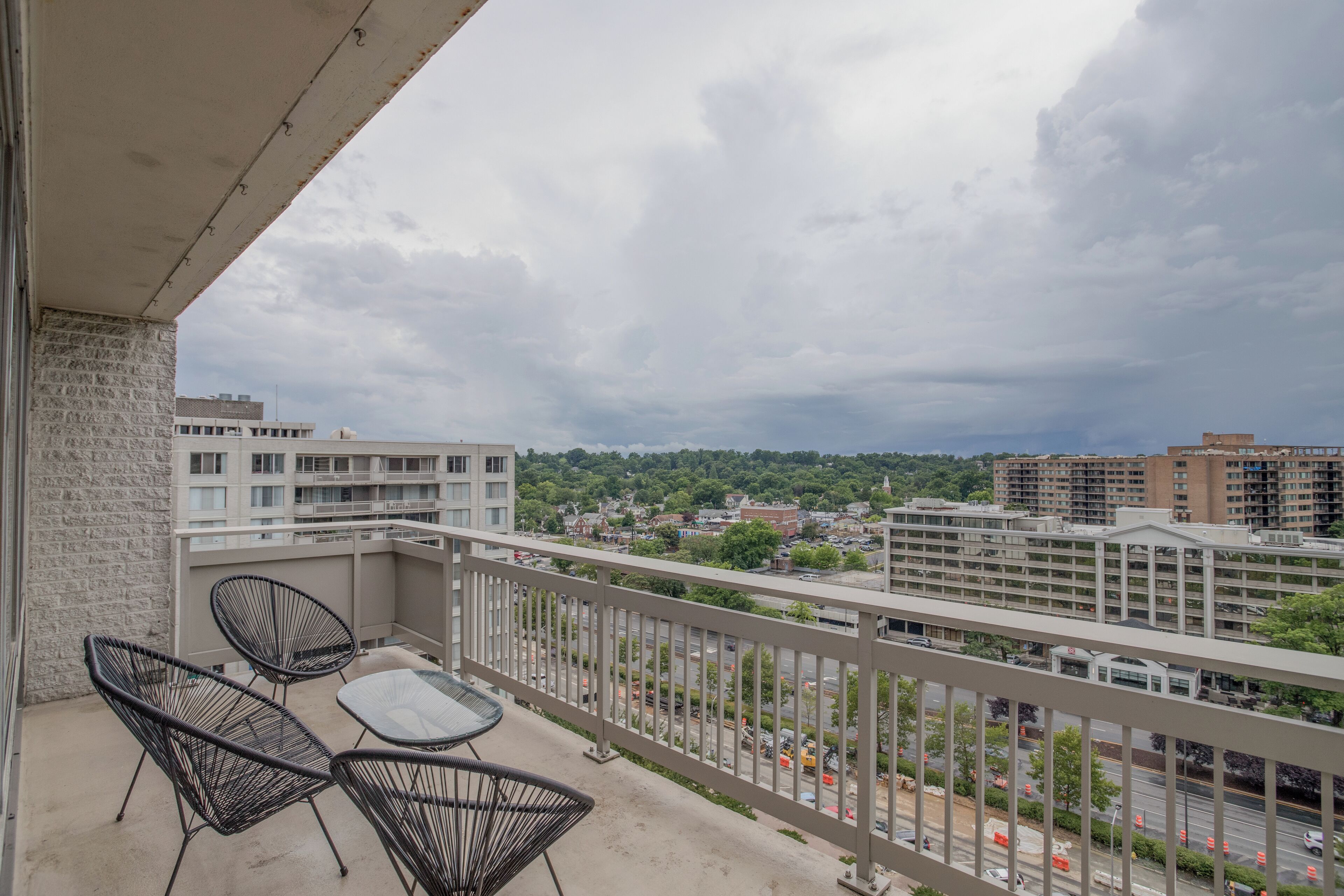 A balcony with a table and chairs, overlooking a cityscape with buildings and a road.