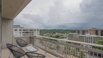 A balcony with a table and chairs, overlooking a cityscape with buildings and a road.