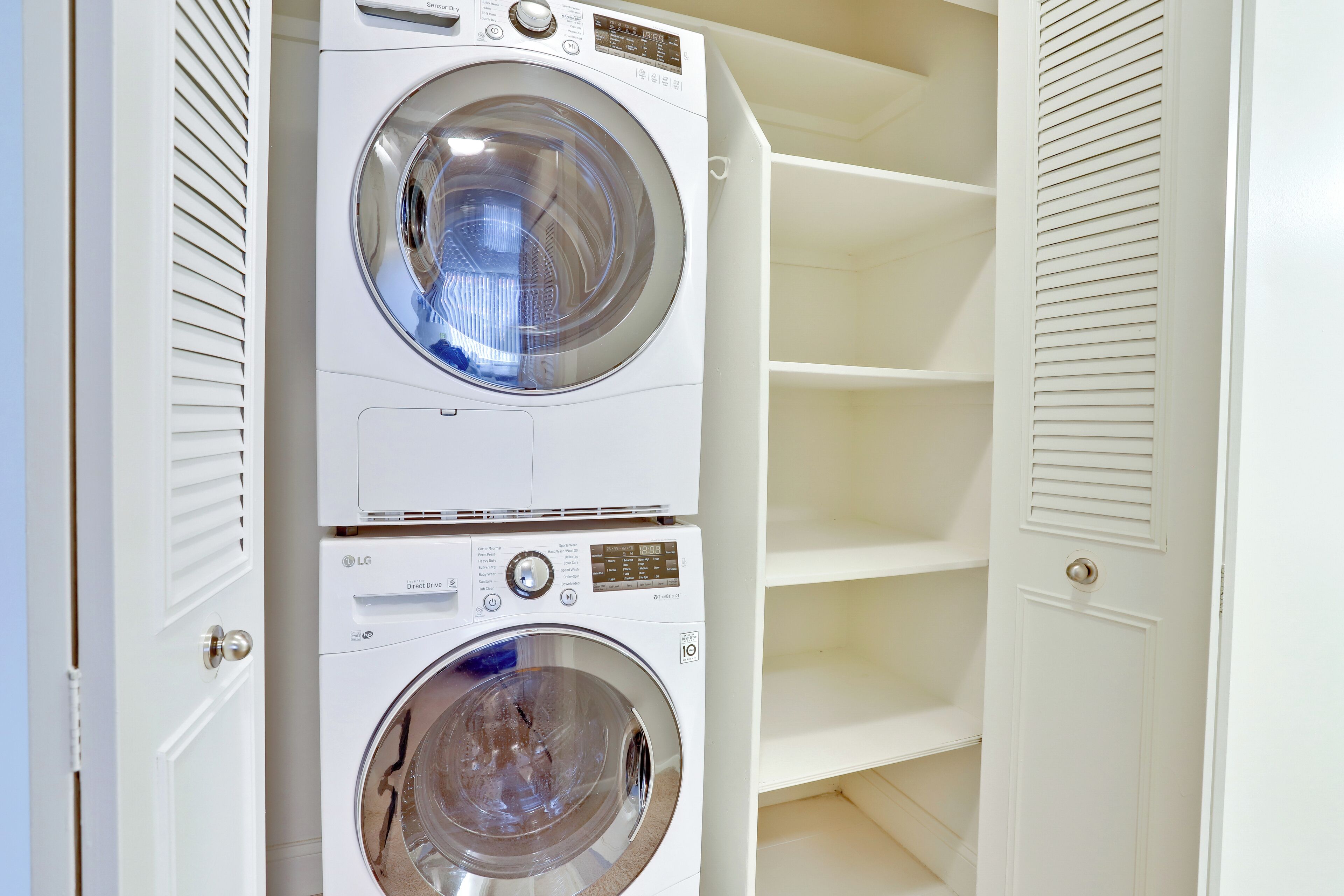A laundry room with two stacked washing machines and a white shelving unit.